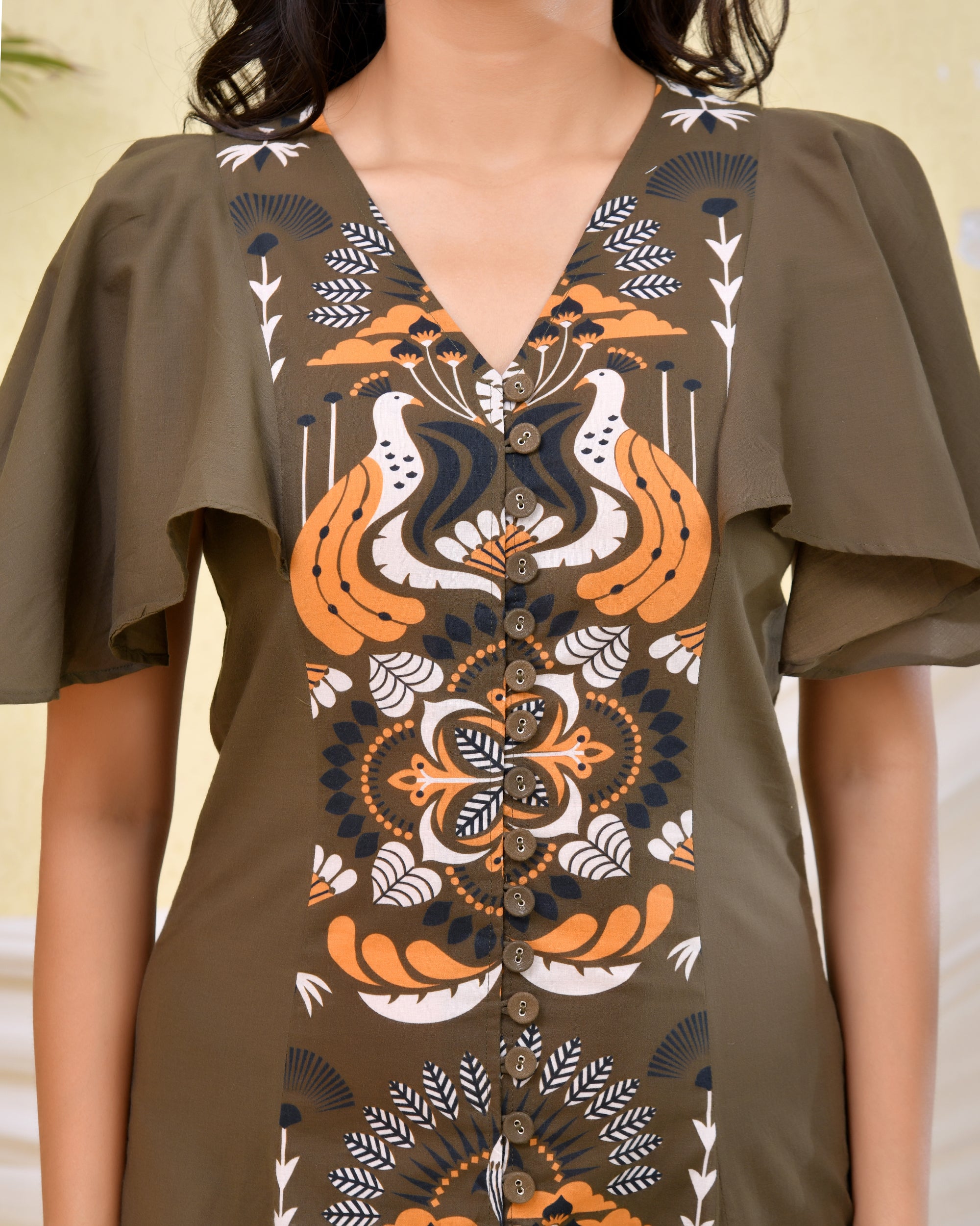 Woman wearing an olive green A-line midi dress with bold floral and bird print and flared cape sleeves