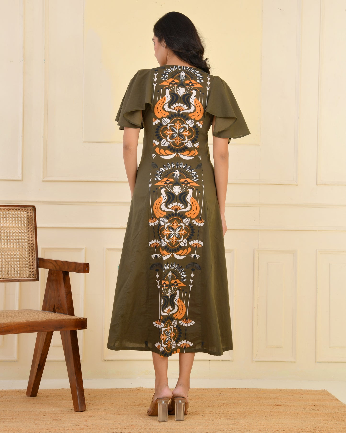 Woman wearing an olive green A-line midi dress with bold floral and bird print and flared cape sleeves