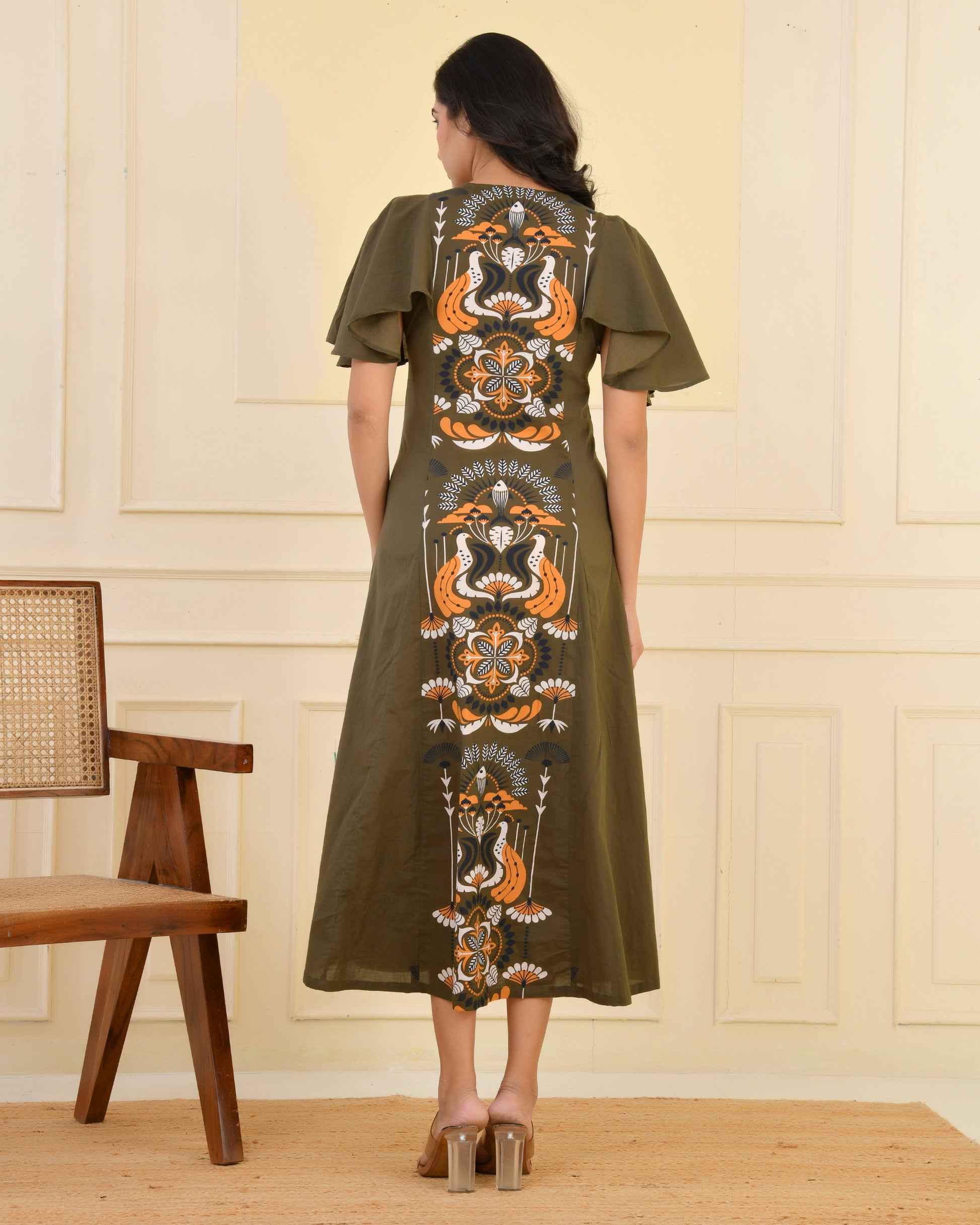 Woman wearing an olive green A-line midi dress with bold floral and bird print and flared cape sleeves